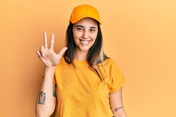 Young hispanic woman wearing delivery uniform and cap showing and pointing up with fingers number three while smiling confident and happy.