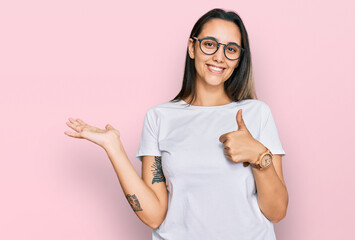 Young hispanic woman wearing casual white t shirt showing palm hand and doing ok gesture with thumbs up, smiling happy and cheerful