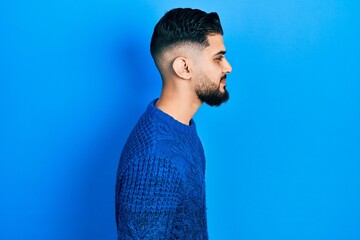 Handsome man with beard wearing casual winter sweater looking to side, relax profile pose with...