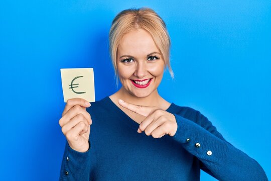 Young blonde woman holding euro symbol reminder smiling happy pointing with hand and finger