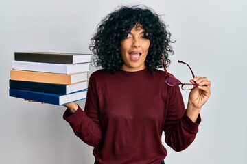 Young hispanic woman holding glasses and books winking looking at the camera with sexy expression,...