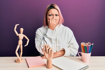 Hispanic woman with pink hair sitting at art studio looking stressed and nervous with hands on...
