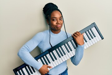 African american woman with braided hair holding piano keyboard depressed and worry for distress,...
