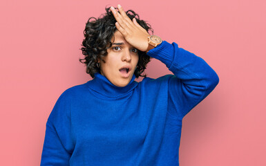 Fototapeta na wymiar Young hispanic woman with curly hair wearing turtleneck sweater surprised with hand on head for mistake, remember error. forgot, bad memory concept.