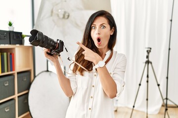 Beautiful caucasian woman working as photographer at photography studio surprised pointing with...