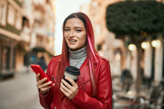Young caucasian girl smiling happy using smartphone and drinking coffee at the city.