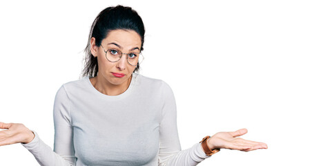 Young hispanic woman wearing casual clothes clueless and confused expression with arms and hands...