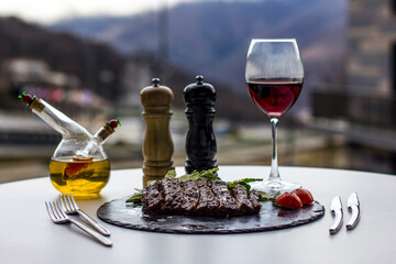 Lunch overlooking the mountains. A glass of red wine. Grilled meat and vegetables. Sweet and sour honey sauce. Stone tray