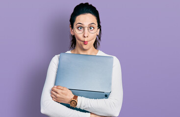 Young hispanic woman working using computer laptop making fish face with mouth and squinting eyes, crazy and comical. - obrazy, fototapety, plakaty