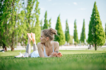 Fototapeta na wymiar Attractive sportive girl lies on the grass and relaxes in park