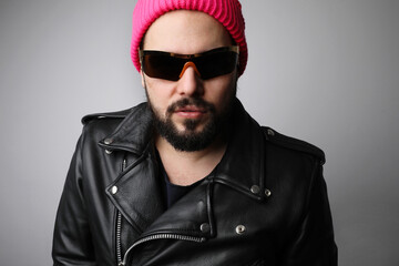 Obraz premium Portrait of bearded man wears leather jacket and sunglasses over white wall.