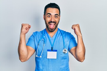 Handsome hispanic man with beard wearing doctor uniform screaming proud, celebrating victory and success very excited with raised arms
