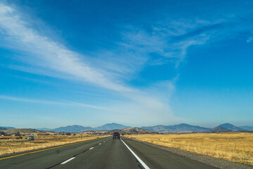 Two lane road in the arid Sierra Nevada's leading to mountains against blue sky