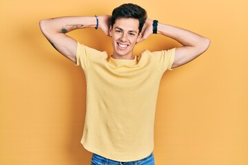 Young hispanic man wearing casual yellow t shirt relaxing and stretching, arms and hands behind head and neck smiling happy