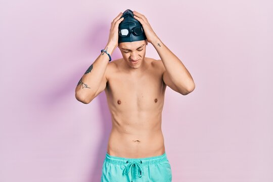Young hispanic man wearing swimwear and swimmer glasses suffering from headache desperate and stressed because pain and migraine. hands on head.