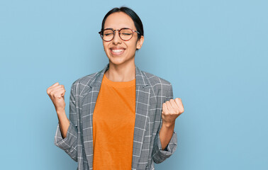 Young hispanic girl wearing business jacket and glasses very happy and excited doing winner gesture...