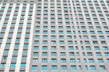 Depressive facade of a modern residential skyscraper. Rows of windows and monotonous brown colors. Photo from the lower angle. Texture or background