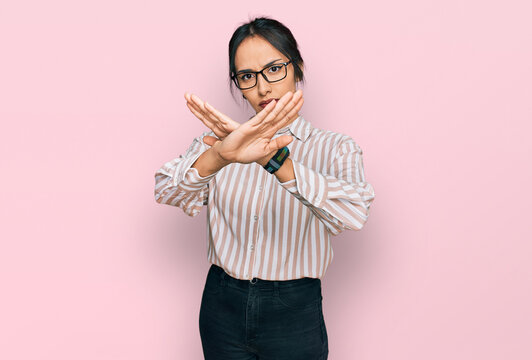 Young hispanic girl wearing casual clothes and glasses rejection expression crossing arms and palms doing negative sign, angry face