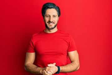 Young hispanic man wearing casual red t shirt with hands together and crossed fingers smiling relaxed and cheerful. success and optimistic