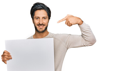 Young hispanic man holding blank empty banner pointing finger to one self smiling happy and proud