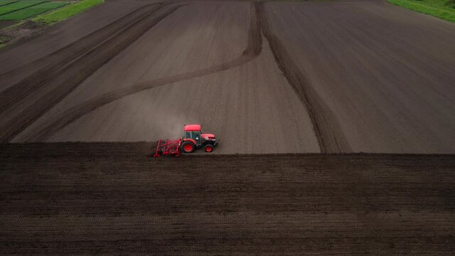 Aerial shot of tractor plowing a small field with blowing dust in the countryside of a small town.