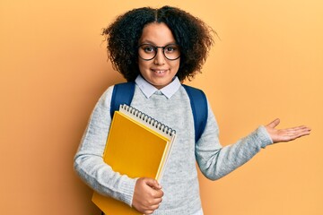 Young little girl with afro hair wearing school bag and holding books celebrating achievement with happy smile and winner expression with raised hand