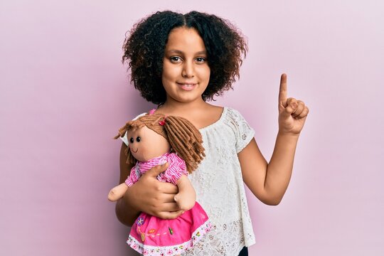 Young little girl with afro hair holding animal doll toy smiling with an idea or question pointing finger with happy face, number one