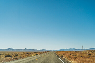 Fototapeta na wymiar Desert highway road leading to the horizon against clear blue sky and mountains