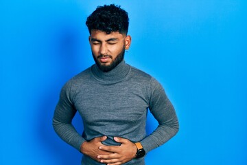 Arab man with beard wearing turtleneck sweater with hand on stomach because indigestion, painful...