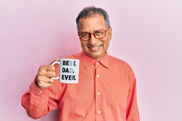 Middle age indian man drinking mug of coffee with best dad ever message looking positive and happy...