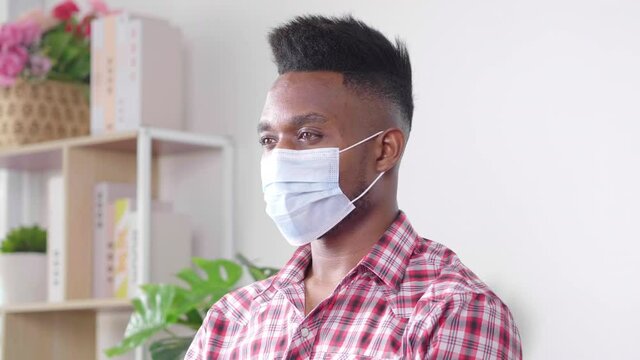 African Man Wearing Mask Sitting Down On A Sofa At Home. Trying To Protect Virus And Pollution. Feeling Bored And Fear Disease. Coronavirus Quarantine