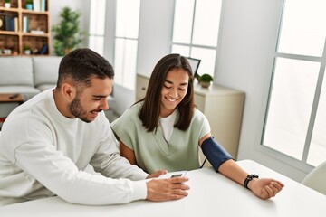 Young latin couple smiling happy measuring blood pressure using tensiometer at home.