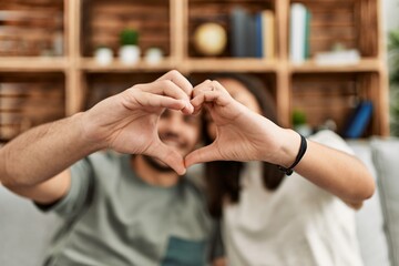Young latin couple smiling happy doing heart symbol with hands at home.