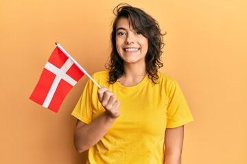 Young hispanic woman holding denmark flag looking positive and happy standing and smiling with a...