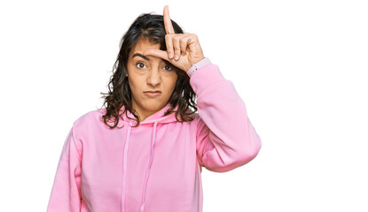 Young hispanic woman wearing casual sweatshirt making fun of people with fingers on forehead doing loser gesture mocking and insulting.