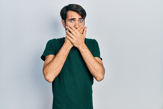 Young hispanic man wearing casual white tshirt shocked covering mouth with hands for mistake. secret concept.