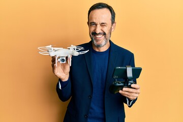 Middle age hispanic man using drone winking looking at the camera with sexy expression, cheerful...