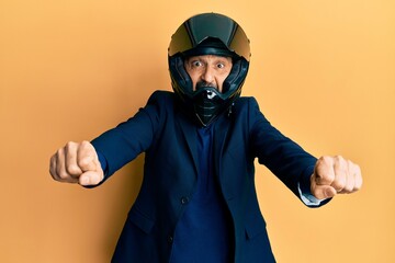 Middle age hispanic man wearing motorcycle helmet doing moto symbol with hands celebrating crazy and amazed for success with open eyes screaming excited.