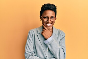 Young african american girl wearing business jacket and glasses looking confident at the camera smiling with crossed arms and hand raised on chin. thinking positive.