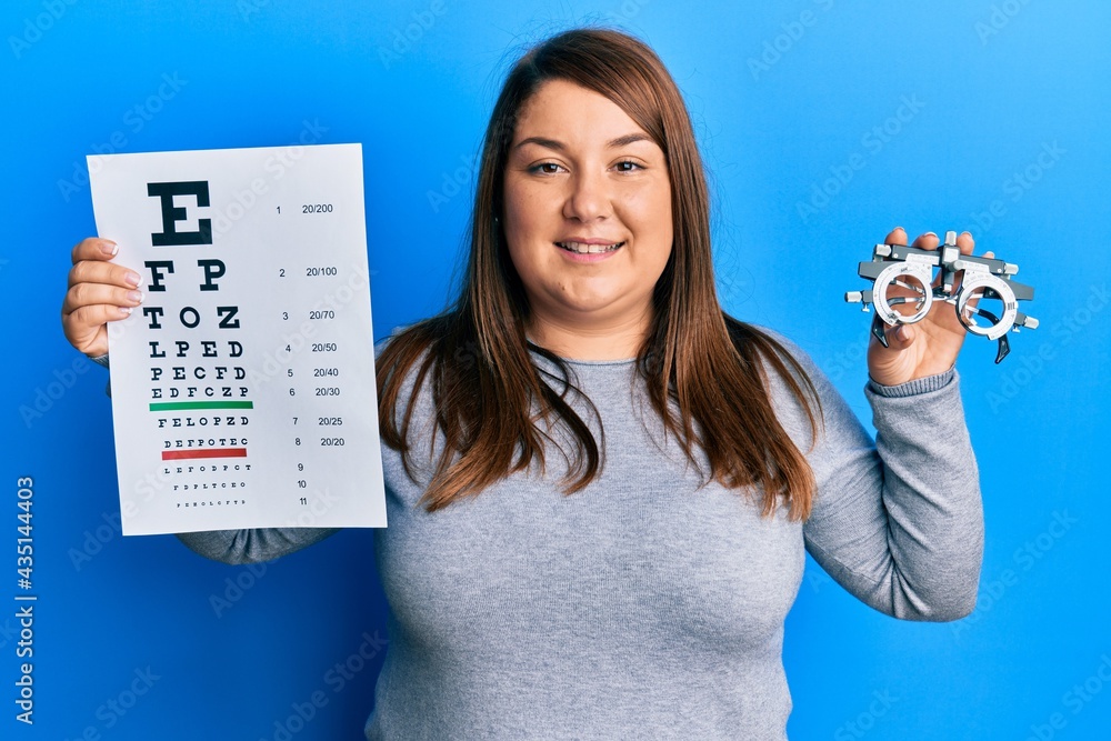 Wall mural Beautiful brunette plus size woman holding optometry glasses and eyesight test smiling with a happy and cool smile on face. showing teeth.