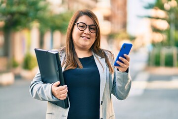 Young plus size businesswoman using smartphone holding binder at the city