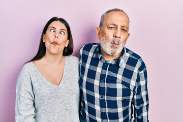 Hispanic father and daughter wearing casual clothes making fish face with lips, crazy and comical gesture. funny expression.