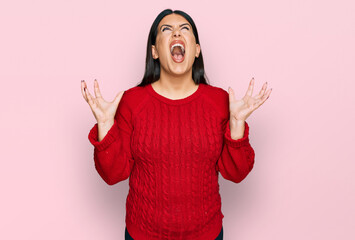 Beautiful brunette woman wearing casual sweater crazy and mad shouting and yelling with aggressive...