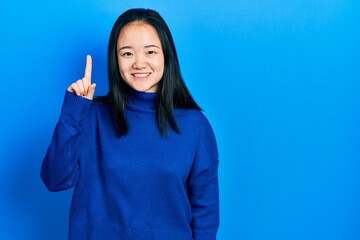 Young chinese girl wearing casual clothes showing and pointing up with finger number one while smiling confident and happy.