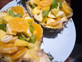 Wonderful fruit salad with a hollowed out pineapple half serving as a container and inside pieces of apple, orange, kiwi, banana and pineapple