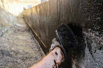 Protective waterproofing coating of walls in contact with the ground with bituminous mastic. Worker...