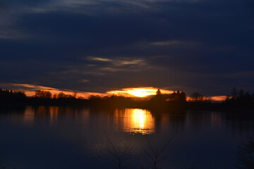 Fototapeta na wymiar Silhouette sunset behind trees is mirroring on lake water