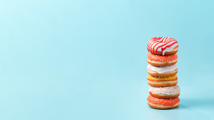Stack of assorted donuts on blue background. Many colorful glazed doughnut with sprinkles stacked with copy space. Long horizontal banner