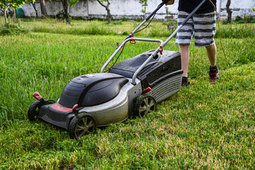 Mowing the lawn with an electric lawnmower. Work in the garden. Temporary job. Ecology. Education of youth.