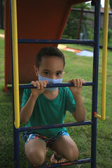 Obraz premium salvador, bahia, brazil - may 15, 2021: child plays in a playground using chewing protection against the coronavirus in the city of Salvador.